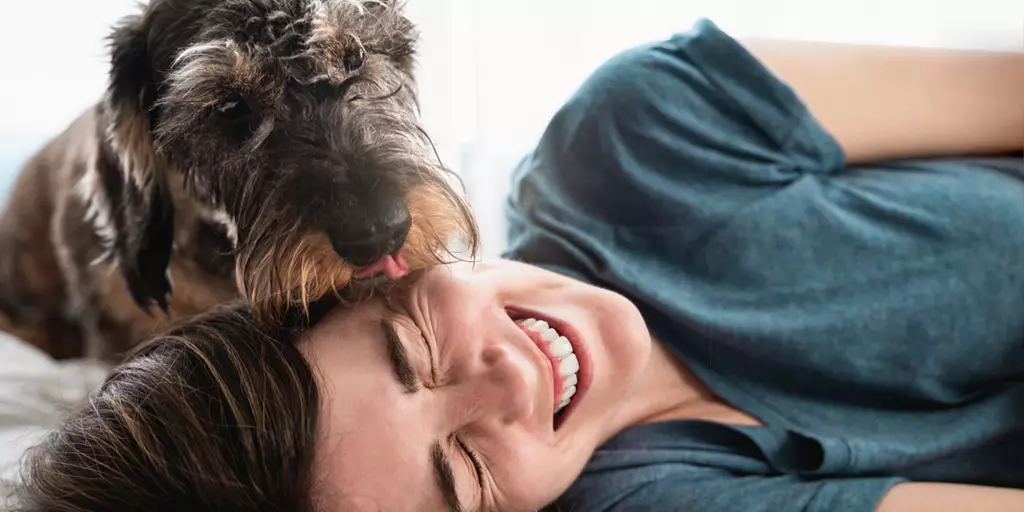 A pet parent in good mental health as her dog licks her face.